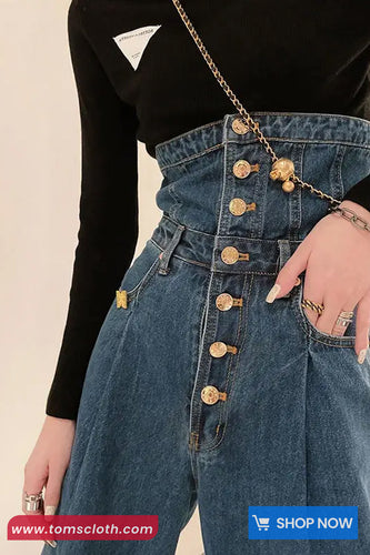 Person wearing a black top and blue denim jumpsuit with gold buttons on a beige background.