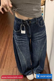 Person wearing blue jeans with a visible brand tag, standing on a wooden floor.