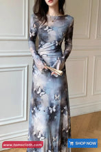 Woman wearing a long, sheer dress with butterfly patterns against a white paneled wall.