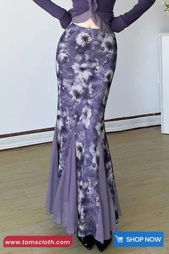 Person wearing a long, patterned purple dress against a white wall.