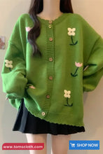 Green cardigan with floral patterns worn by a person, against a plain background.