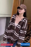 Person wearing a brown and white striped cardigan and cap indoors.