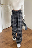 Person wearing a white ribbed top and plaid pants standing in a room with wooden flooring.