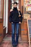 Woman wearing a black off-shoulder sweater and blue jeans standing in front of a store entrance.