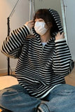 Person wearing a black and white striped hoodie and blue jeans, sitting indoors.