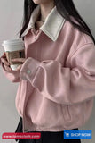 Person wearing a pink jacket with a white collar, holding a coffee cup against a plain background.