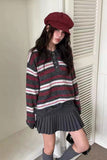 Person wearing a striped sweater and pleated skirt with a maroon cap indoors.