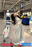 Person in a store with a shopping cart, wearing a white top and light blue jeans.