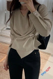 Person wearing a beige wrap top and black pants, holding a phone.