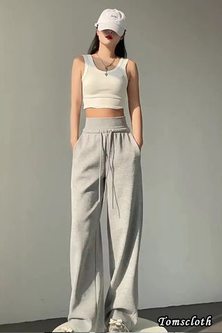 Person wearing a white sleeveless top and gray high-waisted pants against a plain background.