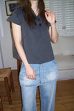 Person wearing a dark blue top and light blue jeans in a room with a couch and wooden floor.
