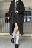 Person wearing a long black coat, skirt, and white socks standing on a tiled floor.