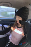 Person sitting in a car wearing a black knit hat and pink shirt with visible branding.