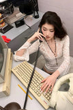 Woman sitting at a desk with a vintage computer, typing and talking on the phone.