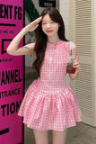 Woman in a pink checkered dress holding a drink, standing in front of a pink sign with text.