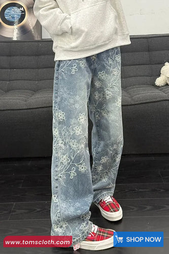 Person wearing light blue floral jeans with a gray couch and records in the background