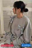 Person wearing a gray sweatshirt with bows sitting indoors.