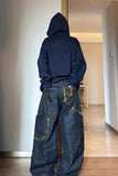 Person wearing a navy hoodie and blue jeans with camouflage patches in a room.