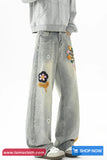Light gray jeans with floral patches worn by a person on a white background, with 'tomscloth.com' branding.
