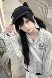Person wearing a black cap and checkered shirt with a graphic design.