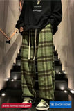 Person wearing a black hoodie and green plaid pants on a staircase with 'tomscloth.com' branding.