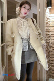 Woman wearing a cream-colored coat with a textured wall and door frame in the background