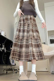 Person wearing a brown plaid skirt with a white shirt and sweater vest indoors.