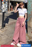 Woman in white crop top and red checkered pants standing on a street.