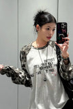 Person wearing a white and camouflage long-sleeve shirt with text, holding a phone with a colorful case.