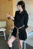 Woman in a black dress with a leopard print belt holding a drink in a casual setting.