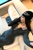 Person wearing a black beanie with text, lying on a beige couch.