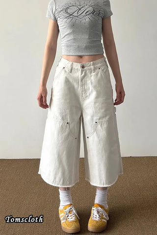 Person wearing a gray crop top, white wide-leg pants, and yellow sneakers on a plain background.