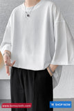 Person wearing a white oversized shirt and black pants against a gray wall with 'tomscloth.com' branding.