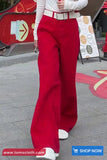 Person wearing red pants and a white top on a sidewalk with a store sign in the background.