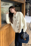 Woman wearing a cream-colored cardigan with black buttons, holding a black handbag, standing on a wooden deck.