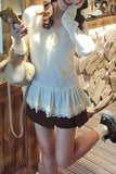 Woman wearing a white lace top and brown shorts, holding a phone, with a stone wall and wooden floor in the background.