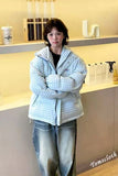 Person wearing a checkered jacket and jeans standing in a store setting with shelves and products.