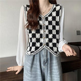 Person wearing a black and white checkered vest over a white shirt and blue jeans.