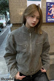 Person wearing a gray jacket standing outdoors near a building with posters on the wall.