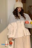 Person wearing a white outfit with a beige hat, holding fruits indoors.