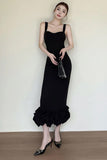 Woman wearing a black dress with ruffled hem against a white wall.