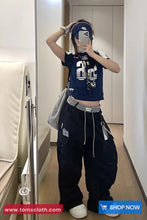 Person taking a mirror selfie wearing a navy blue t-shirt with white graphics and dark pants, holding a phone.