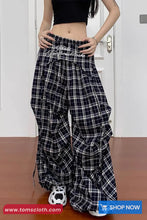 Person wearing black and white plaid pants with a visible brand logo, standing against a white door.