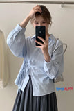 Person wearing a light blue shirt with rolled-up sleeves and a dark skirt, taking a mirror selfie.