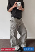 Person wearing gray cargo pants and a dark shirt, holding a phone against a plain background.