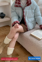 Person sitting on a couch wearing a light blue puffer jacket with plaid lining, reading a book.