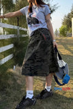 Person wearing a graphic t-shirt, camouflage shorts, and black sneakers outdoors.