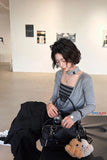 Woman sitting on a bench in an art gallery holding a black handbag with plush toys.