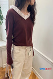 Person wearing a maroon sweater with white lace collar and beige pants, holding a brown bag indoors.