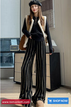 Woman in stylish outfit with striped pants and a vest in an indoor setting.